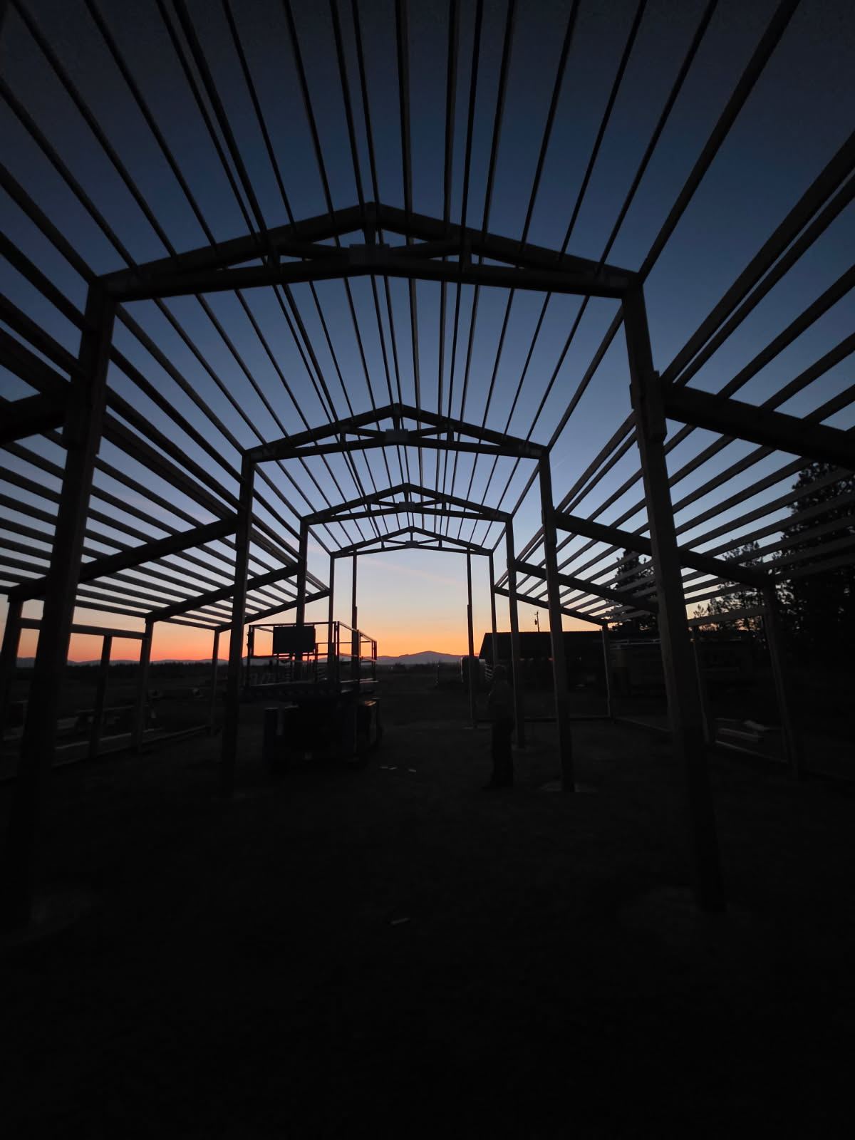 Interior view along the length of the barn frame at sunset, roof purlins in place and open to the sky