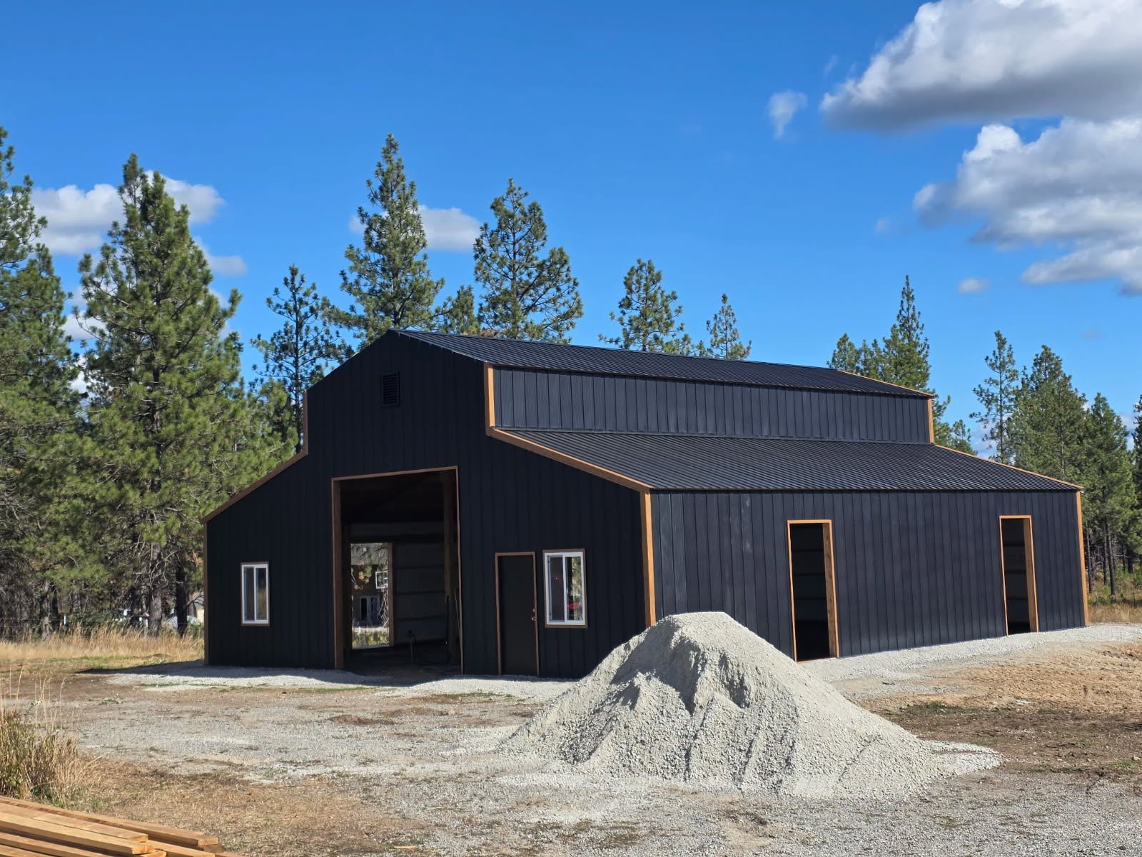 The barn clad in black vertical steel siding and matching roofing, with tan trim around the openings